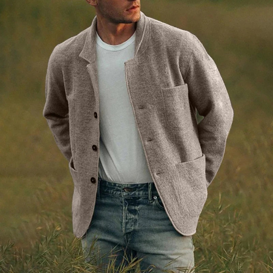 Mann i brun ulljakke og jeans sitter utendørs. Stilig herremote, høstklær, casual stil. Perfekt for kjølige dager.