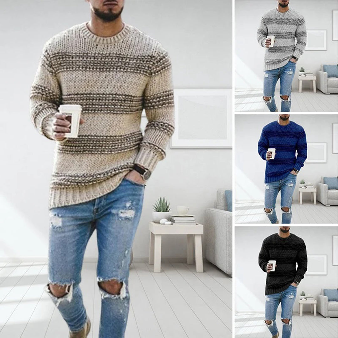 Mann iført LANDYN-strikket genser i beige, grå, blå og svart, med kaffekopp. Perfekt for høst- og vintermote. Komfortabel og stilfull genser.